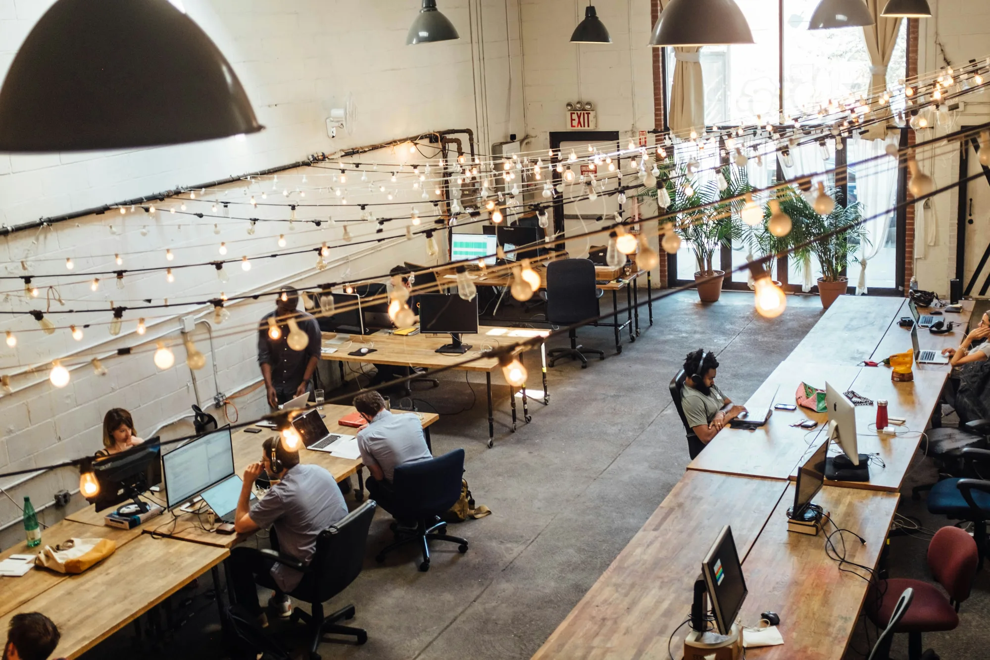 Bright industrial coworking space with long work tables and warm lighting